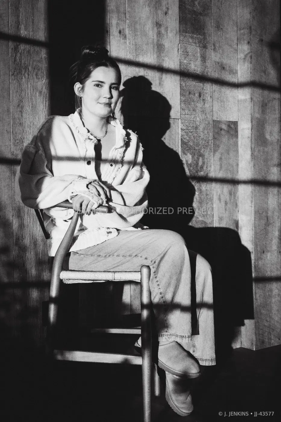 Black-and-white portrait of a seated woman crossed by window shadows