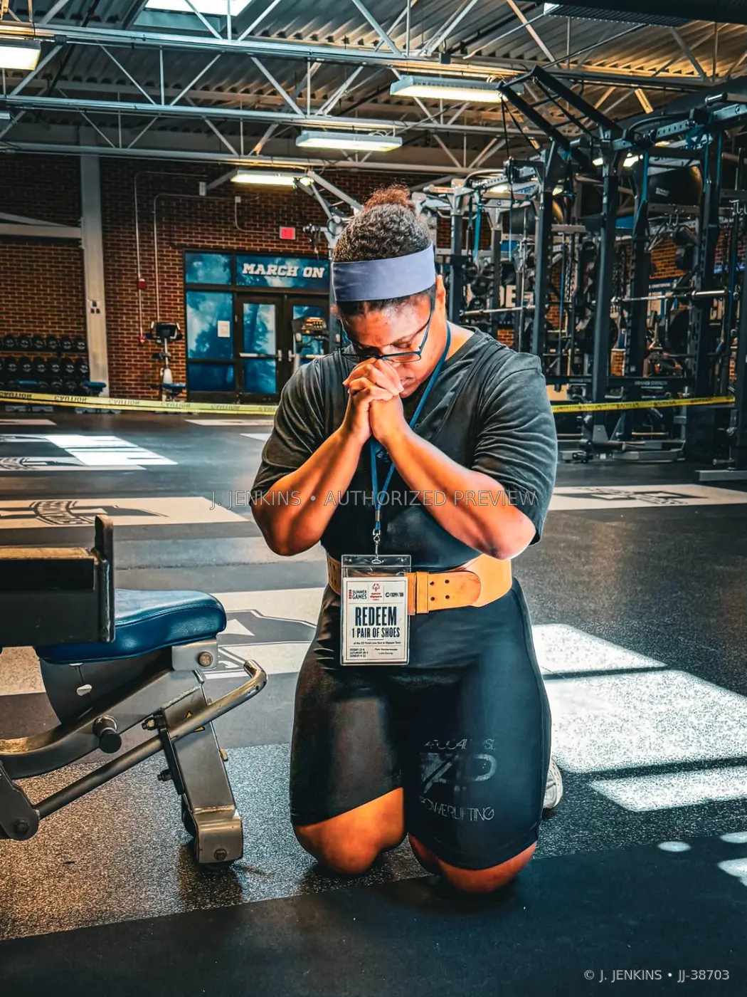 Powerlifter kneeling in focused reflection inside an industrial training hall