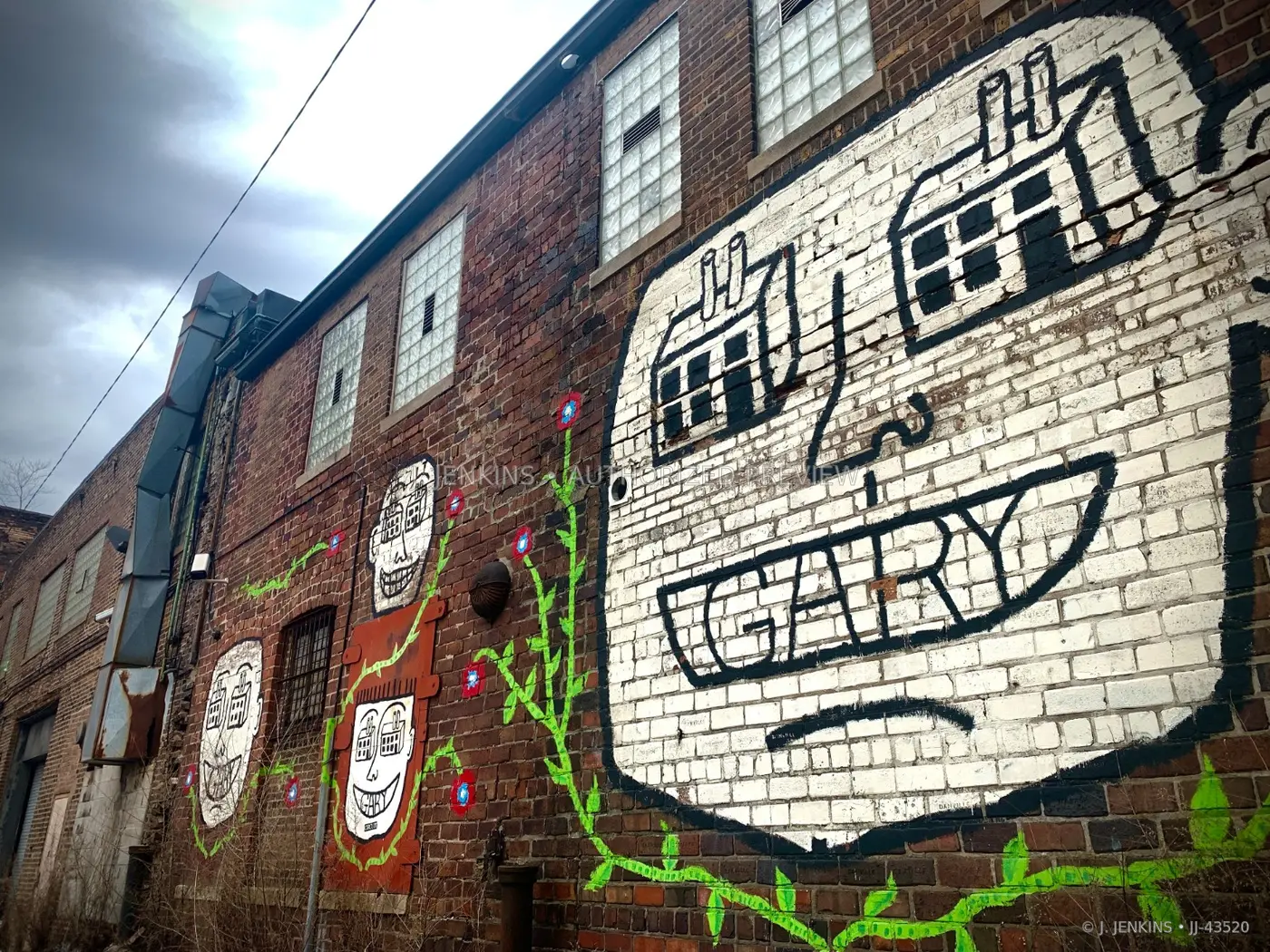 Faces and green vines painted across an old brick building